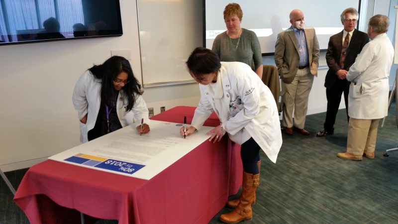 From left, Dr. Hemangini Shah, a radiation oncologist, and Dr. Desiree D'Angelo-Donovan, a surgeon, sign the "80 by 2018" pledge card.